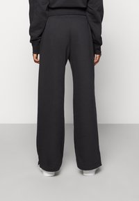 Czarne długie spodnie dresowe o gładkiej teksturze, z elastycznym paskiem w talii i subtelnymi detalami szwów na końcach. Stylizowane z białym obuwiem.