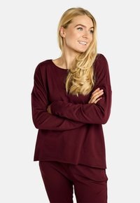 Bordo majica z dolgimi rokavi s sproščenim krojem, okroglim izrezom in mehko teksturo. Kombinirana z usklajenimi hlačami, ki izkazujejo preprost dizajn.