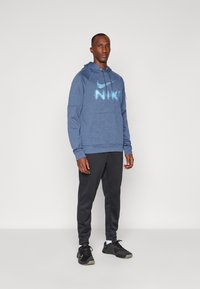 Námornícky sveter s veľkým, svetlo modrým logom Nike, skombinovaný s čiernymi teplákmi a čiernymi športovými topánkami s akcentami Nike.
