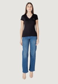 Maglietta nera in cotone con scollatura a V e maniche corte, abbinata a jeans di denim blu chiaro. Design aderente con un logo discreto sul petto.