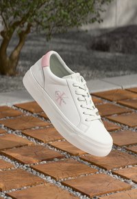 Bijele tenisice s ružičastim detaljem na peti, s gornjim dijelom od glatke kože, ravnim vezicama i blago povišenom bijelom potplatu; sadrže Calvin Klein logo.
