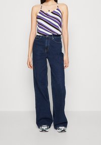 Canottiera leggera a righe in viola, blu e nero abbinata a jeans in denim blu scuro a vita alta e gite larghe, con sneakers grigie.