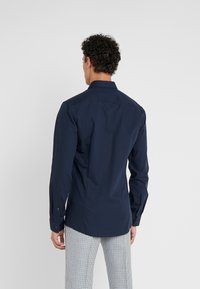 Camisa de manga larga de color navy con cuello extendido, textura suave y puños con botones, combinada con pantalones de patrón de espiga.