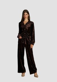 Set di abbigliamento da casa in velluto marrone, composto da una camicia con bottoni a vestibilità rilassata e pantaloni a gamba larga. Tessuto liscio con finitura lucida.