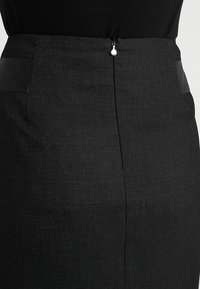 Svart blyertskjol med en texturerad yta, släta läderliknande detaljer på fickorna och en diskret dragkedjestängning i ryggen.