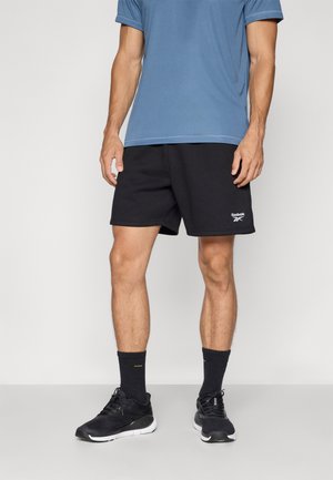Shorts sportivi neri con una texture liscia e logo bianco; abbinati a una maglietta a maniche corte blu e scarpe da running nere.