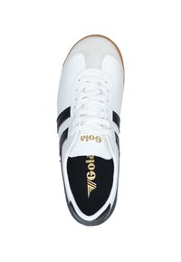 Zapatilla deportiva blanca con rayas negras, puntera de ante y suela de goma. Presenta una plantilla negra con marca dorada.