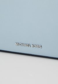 Sac en cuir bleu clair avec une texture lisse et un logo argenté en relief "MICHAEL KORS". Accents bleu foncé le long des bordures.