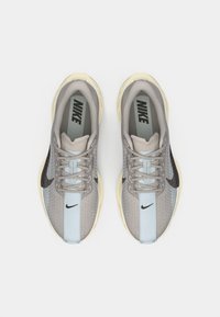 Par de zapatillas de correr Nike en beige y azul claro con logotipos negros de la marca, cordones grises y suelas color crema, vista desde arriba sobre un fondo blanco.