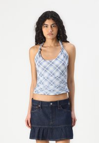 Top corto halter a cuadros azules con textura recogida, combinado con una falda de mezclilla oscura que presenta un dobladillo con volantes y bolsillos delanteros.