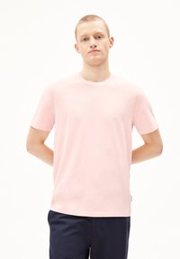 Lichtroze katoenen T-shirt met korte mouwen, ronde hals en een rechte snit. Soepele textuur met een labeldetail aan de linkerkant nabij de zoom.