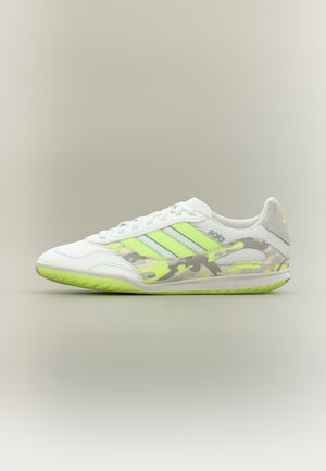 Zapatilla deportiva blanca con rayas verde neón, detalles con patrón de camuflaje y suela verde neón sobre un fondo neutro, vista lateral hacia la izquierda.
