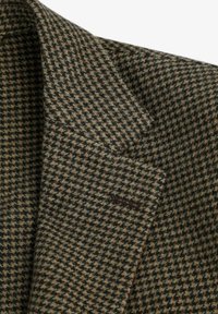 Blazer de tweed en patrón de espiga marrón y verde, con solapa en pico, bolsillo en el pecho y tejido texturizado con fibras visibles.