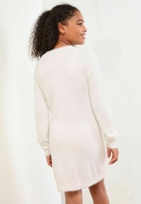 Weißes, flauschiges Strickkleid mit langen Ärmeln, Rundhalsausschnitt und lockerer Passform, das eine weiche Textur und eine Länge bis zur Mitte des Oberschenkels aufweist.