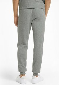 Pantalones de chándal gris de algodón con puños acanalados, cintura elástica y un corte relajado, combinados con zapatillas blancas sobre un fondo neutro.