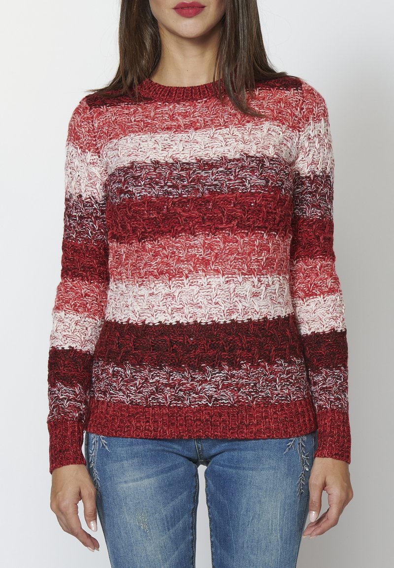 Sweter dziany w poziome czerwone, różowe i białe paski. Posiada teksturowany wzór oraz ściągacze przy dekolcie i rękawach. Połączony z dżinsami.