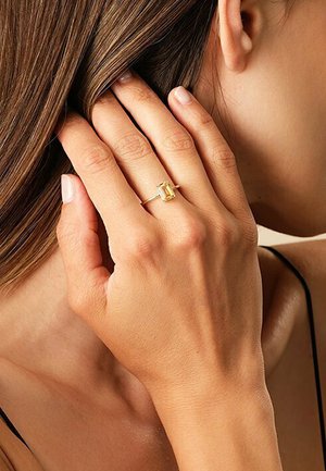 Goldring mit einem smaragdgeschliffenen gelben Stein, auf einem schlanken Band gesetzt. Hand in der Nähe der Haare positioniert, zeigt den Hautton und die Details des Rings.