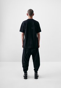 Black oversized short-sleeve shirt and baggy pants, made of a textured fabric, featuring a back seam and subtle logo details.
