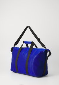 Blue duffel bag made of shiny, durable fabric, featuring black adjustable straps and handles, rectangular shape, and seamless exterior.