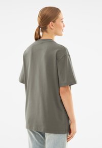Oversized, korte mouwen t-shirt in donkergroen katoen. Ronde halslijn, rechte zoom en een zachte textuur. Geen zichtbare graphics of versieringen.