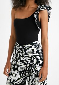 Bodysuit noir à côtes avec une épaule dénudée et un motif floral froncé. Pantalons taille haute noir et blanc à motifs floraux avec détail de bouton.