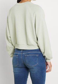 Sweat-shirt vert clair, oversize, avec ourlet et poignets côtelés, associé à un jean denim bleu moulant avec poches arrière.