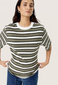 Camiseta a rayas verdes y blancas de manga corta, con un cuello blanco acanalado y un ajuste relajado, combinada con jeans de mezclilla azul.