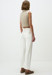 Beige ärmelloses Oberteil mit Kragen, kombiniert mit hochtaillierten weißen Hosen und braunen Slippern, von hinten betrachtet.