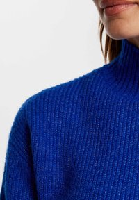 Sweter dzianinowy w intensywnym niebieskim kolorze z wysokim kołnierzem. Posiada żebrową strukturę i miękki, przytulny wygląd.