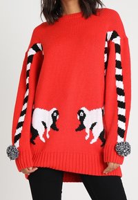 Maglione rosso lavorato a maglia con design di pecore bianche e nere sul davanti e maniche a righe bianche e nere, con dettagli in pom-pom sui polsini.