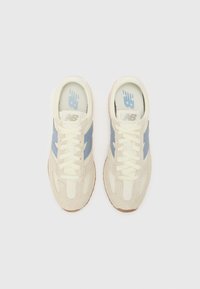 New Balance sneakers feature a cream upper with light blue accents, textile and suede materials, and a rubber sole. Classic lace-up design.