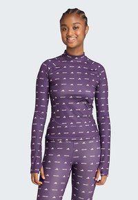 Bluza sportivă mov cu mâneci lungi și guler tip mock neck, cu un model repetitiv de logo-uri albe. Material neted și croială ajustată pentru îmbrăcăminte activă.