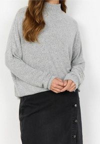 Lys grå, langærmet sweater med høj hals, der har en løs pasform og blød tekstur, parret med en sort denimnederdel med knapdetaljer.