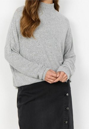 Pull gris clair à manches longues avec un col montant, offrant une coupe débordante et une texture douce, associé à une jupe en denim noire avec des accents de boutons.