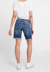 Džínové kraťasy ve středně modrém praní, s ohrnutými lemy, zadními kapsami a mírným vyblednutím. V kombinaci s jednoduchým bílým tričkem a bílými teniskami.