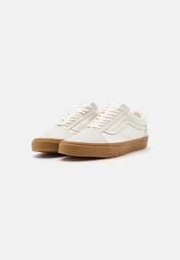 Para kremowych sneakerów niskich z gumowymi podeszwami i białymi sznurowadłami na jednolitym białym tle.