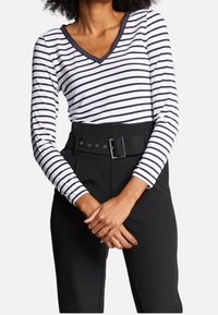 Vit långärmad topp med svarta horisontella ränder, V-ringning med kontrasterande kant, parat med högmidjade svarta byxor med ett bälte.