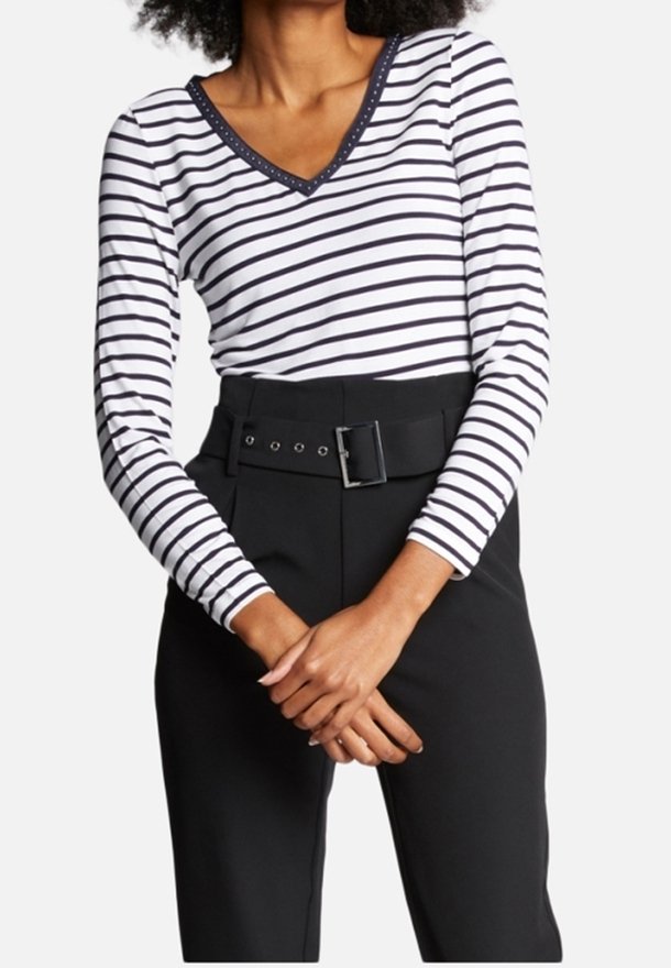 Vit långärmad topp med svarta horisontella ränder, V-ringning med kontrasterande kant, parat med högmidjade svarta byxor med ett bälte.