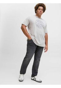 Camiseta de algodón gris claro con un gráfico circular que dice "SUPERIOR Quality GARMENTS", combinada con jeans gris oscuro y zapatillas blancas.