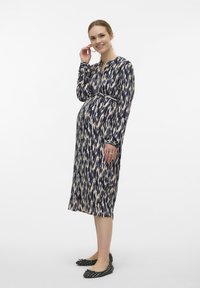 Marinblå och krämfärgad mönstrad gravidklänning med långa ärmar, knäppning vid halsen, midjeband och ankellång längd, matchad med svarta lägenheter.