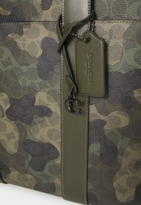 Borsa a tracolla in pelle testurizzata con motivo camouflage verde e nero, dotata di una tracolla in tessuto, etichetta e dettagli in metallo.