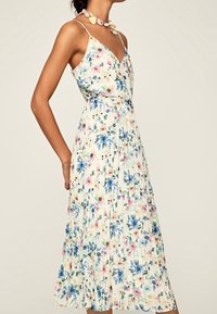 Kwiatowa sukienka midi z dekoltem w serek, cienkimi ramiączkami i zwężoną talią. Charakteryzuje się jasnokremowym tłem, niebieskimi i różowymi kwiatami oraz plisowanym materiałem.