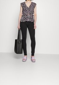 Blouse noire à fleurs avec manches à volants, associée à un jean skinny noir, des sandales à talons carrés lavande et un sac cabas noir.
