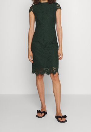 Abito in pizzo verde scuro con maniche corte, orlo smerlato e motivi floreali intricati; abbinato a sandali platform neri.