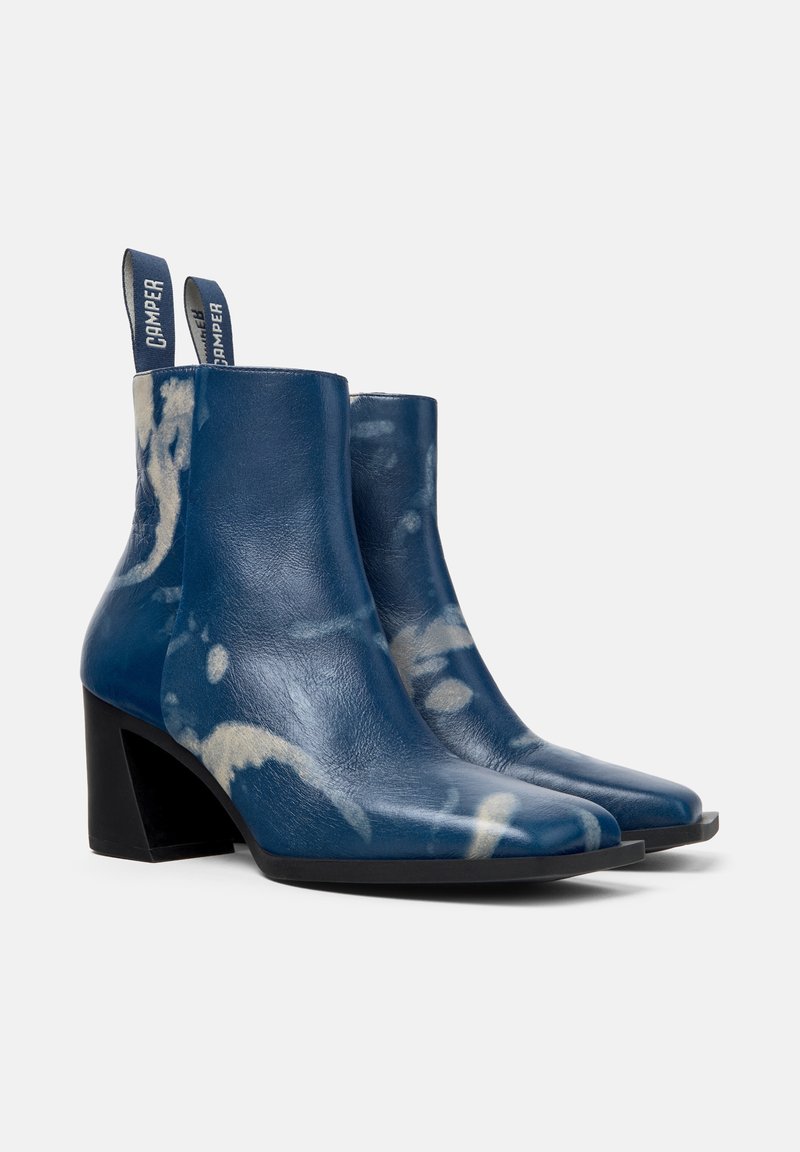 Blå läderankelboots med glansig yta, med ett lätt marmormönster, fyrkantig tå och klack för stabilitet.