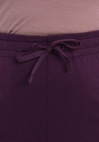 Lila elastisk midjeband med dragsko, som visar en slät textilstruktur. Toppen är i en ljus mauve-färg och är något åtsittande.