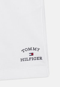 Tessuto bianco con logo Tommy Hilfiger ricamato in testo nero e piccolo emblema rettangolare rosso, bianco e blu.