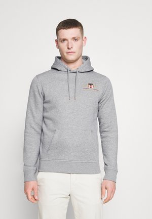 Grå hoodie med kengurulomme, snøre i hætten og broderet emblem. Blødt stof med ribbede manchetter og kant.