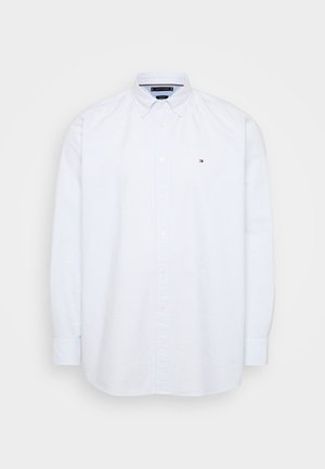 Chemise blanche à boutons avec des rayures verticales bleu clair, manches longues, et un logo Tommy Hilfiger sur le côté gauche de la poitrine. Tissu en coton.