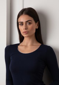 Maglietta a maniche lunghe blu navy con scollatura rotonda, caratterizzata da un accento argento lungo il collo. Tessuto morbido e liscio con una silhouette aderente.